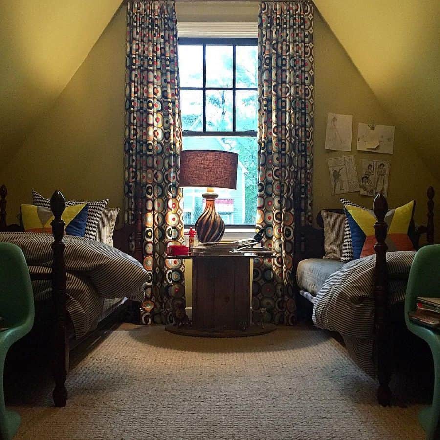 Cozy attic bedroom with twin beds, yellow curtains, and a lamp on a wooden table by the window