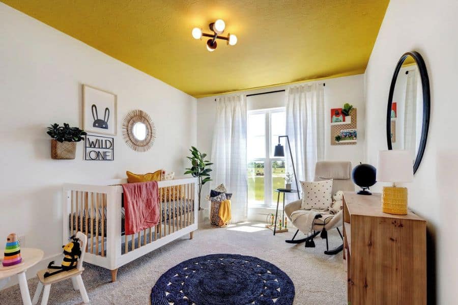 Sunny nursery with yellow ceiling, cozy crib, toys, rocking chair, and a large window with sheer curtains
