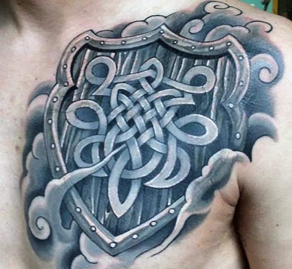 Tattoo of a detailed shield with a knot pattern and cloud-like elements on chest