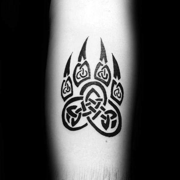 Celtic wolf paw tattoo in solid black ink with triquetra knotwork inside each pad and claw, placed on the inner forearm.
