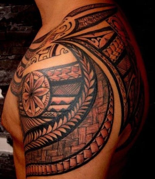 An elaborate black and red traditional tribal tattoo covering a shoulder and arm