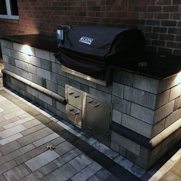 Built-in outdoor stone grill station with stainless steel doors and a covered barbecue under soft lighting