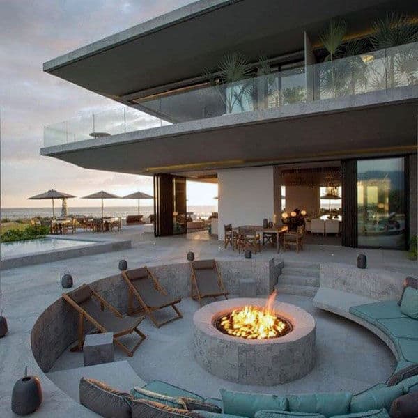 Modern house with beach view, sunken fire pit seating area, and lounge chairs on a concrete patio by the pool
