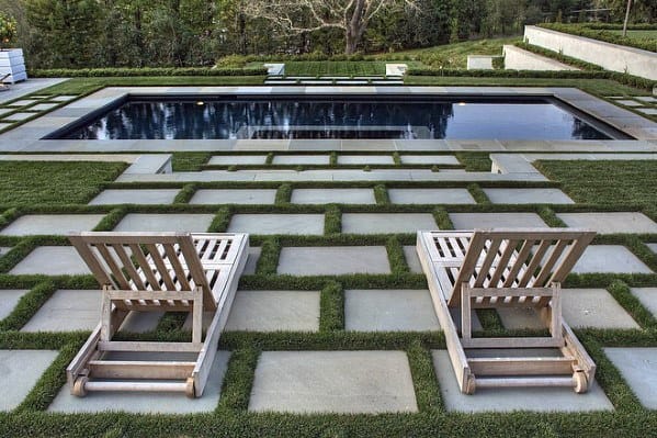 Two wooden lounge chairs facing a rectangular pool, surrounded by geometric stone and grass patterns