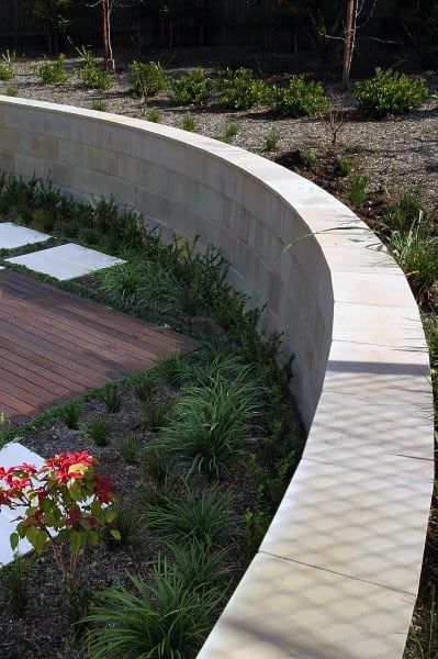 Curved concrete retaining wall with landscaped greenery and adjacent wooden decking.