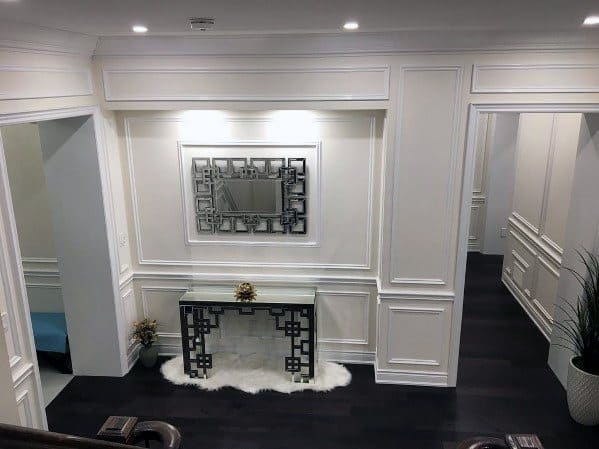 Elegant foyer featuring white chair rail molding, intricate millwork, a geometric mirror, and dark wood flooring