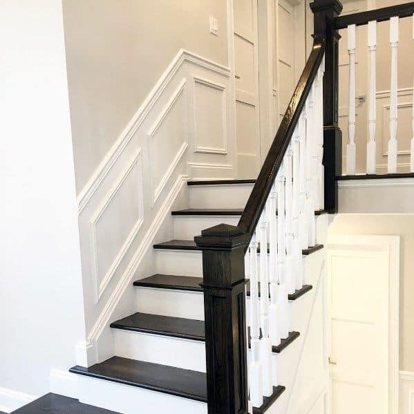 Bright staircase with white chair rail molding, dark wood steps, and contrasting black handrails for a timeless look