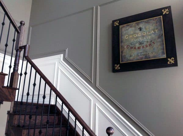 Stylish staircase with gray and white walls, chair rail molding, dark wood steps, and wrought iron railings