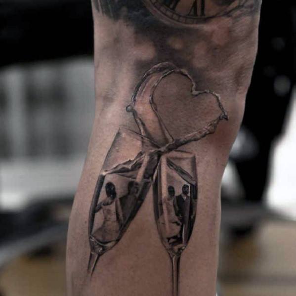 Tattoo of two champagne glasses with splashing liquid forming a heart on a person's arm.