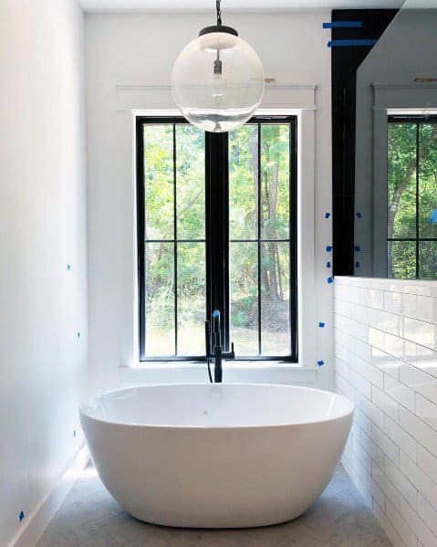 Minimalist bathroom with freestanding tub, large window, and round glass pendant light.