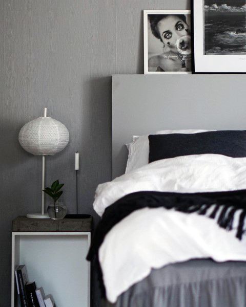 Minimalist bedroom with a grey wall, framed photos, white bed linens, and a small side table with a lamp