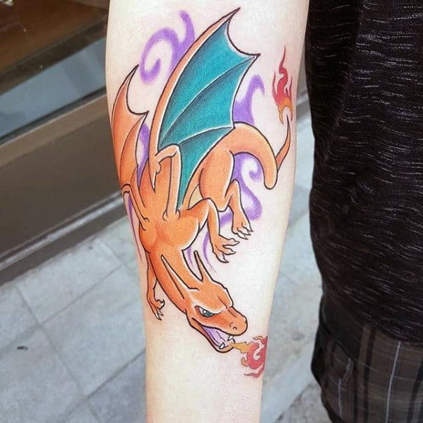 Stylized Charizard tattoo on forearm, with teal wings, swirling purple smoke, and a flame emerging from its mouth.