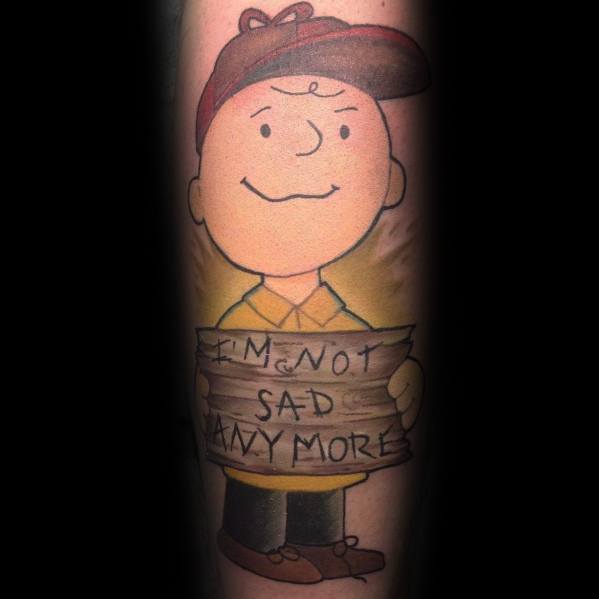 Charlie Brown tattoo with a heartfelt twist, holding a wooden sign that reads 'I'm not sad anymore,' symbolizing resilience and growth.