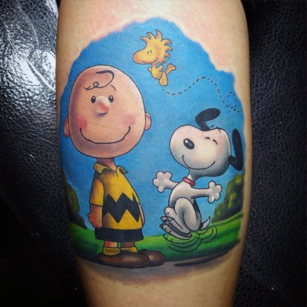 Vibrant Charlie Brown, Snoopy, and Woodstock tattoo set against a bright blue sky, capturing the joy and warmth of Peanuts' friendship.