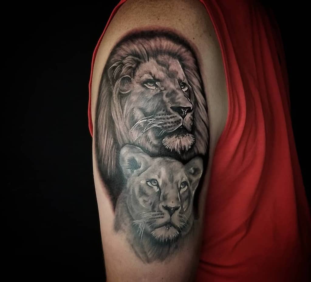 Realistic black and grey tattoo on the upper arm, featuring a majestic lion and lioness with detailed shading for a powerful and symbolic design.