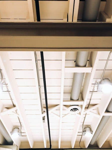 Exposed basement ceiling with painted beams, pipes, and industrial lighting fixtures.
