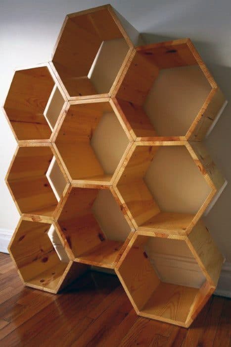 Wooden bookshelf with hexagonal compartments arranged in a honeycomb pattern, placed against a white wall