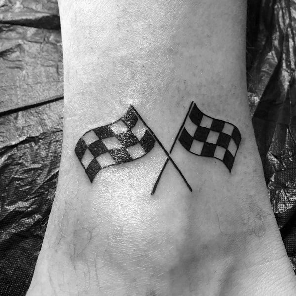 Simple crossed checkered flags tattoo on the ankle, symbolizing victory, racing spirit, and a passion for speed.