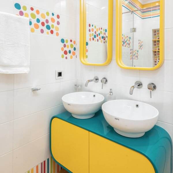Cheerful bathroom with colorful polka dots on white tile, curved teal-and-yellow vanity, and round mirrors above white basins.