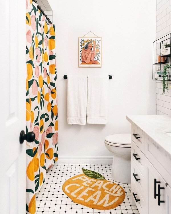 White bathroom featuring a fruity shower curtain, peach-themed mat, black-and-white tile, and a white vanity with black hardware.