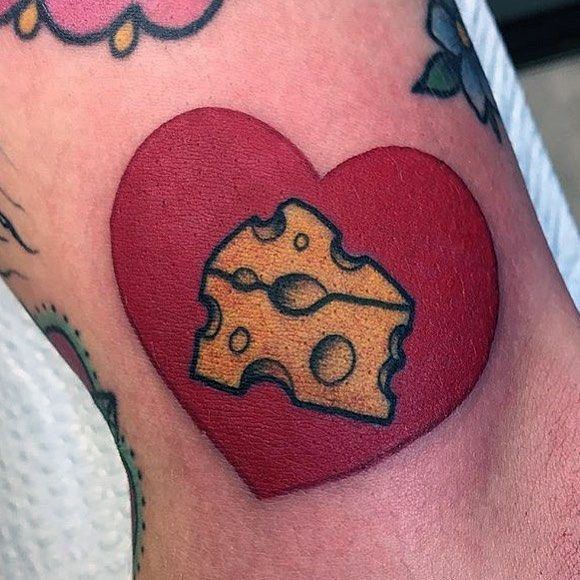 Colorful cheese tattoo featuring a vibrant red heart background with a wedge of Swiss cheese in bold black outlines and yellow shading.