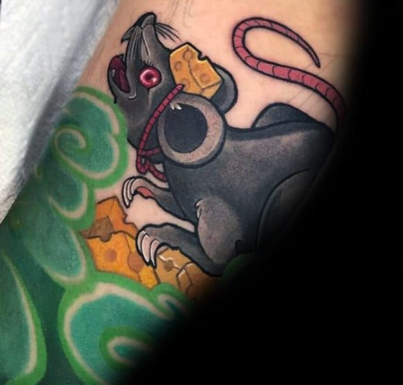 Colorful tattoo of a black rat clutching pieces of cheese, surrounded by green swirling patterns, featuring bold outlines and vivid shading.