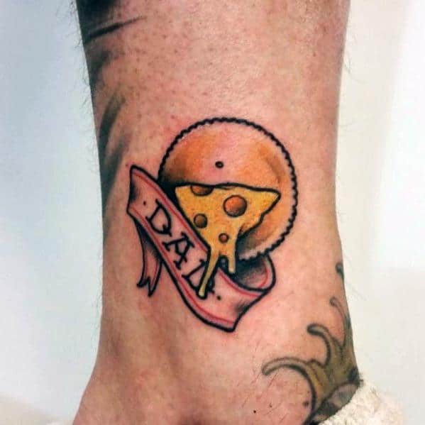 Colorful tattoo of a cheese wedge on a cracker with a ribbon that reads "DAD," featuring bold outlines and warm shading on the ankle.