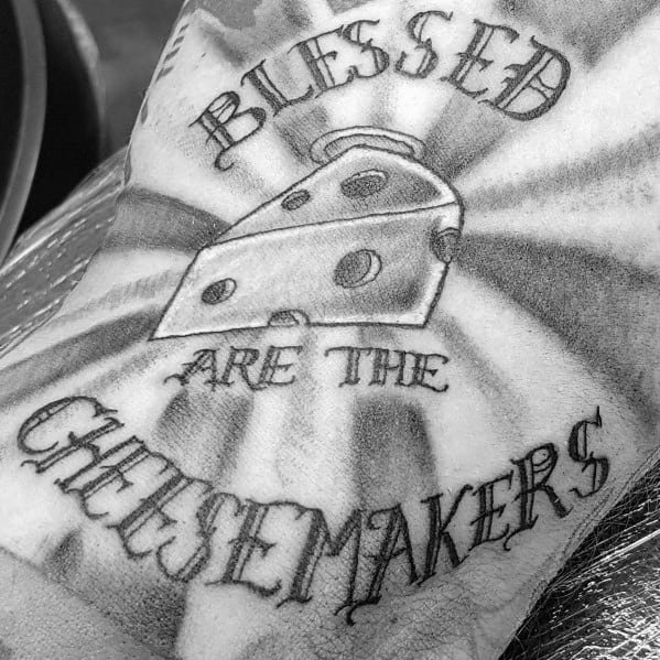 Black and gray tattoo featuring a wedge of Swiss cheese with the phrase "Blessed are the Cheesemakers" in bold, stylized lettering and radiant shading.