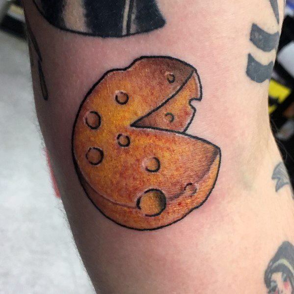 Colorful tattoo of a round cheese wheel with a wedge cut out, featuring bold black outlines, rich yellow-orange shading, and a textured appearance.