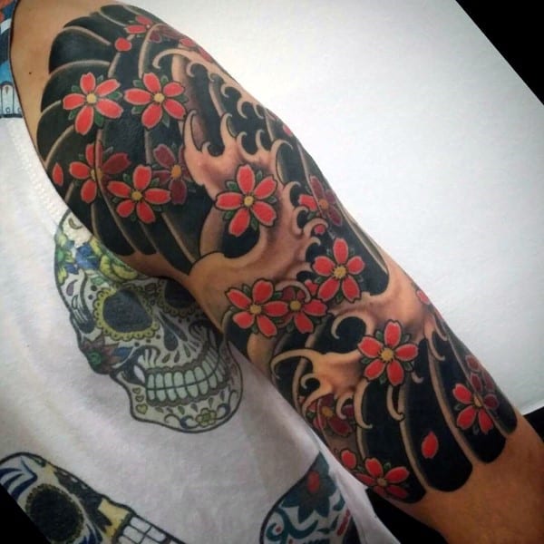 Japanese-style full sleeve tattoo featuring bold black and gold waves with vibrant red cherry blossoms, creating a striking contrast
