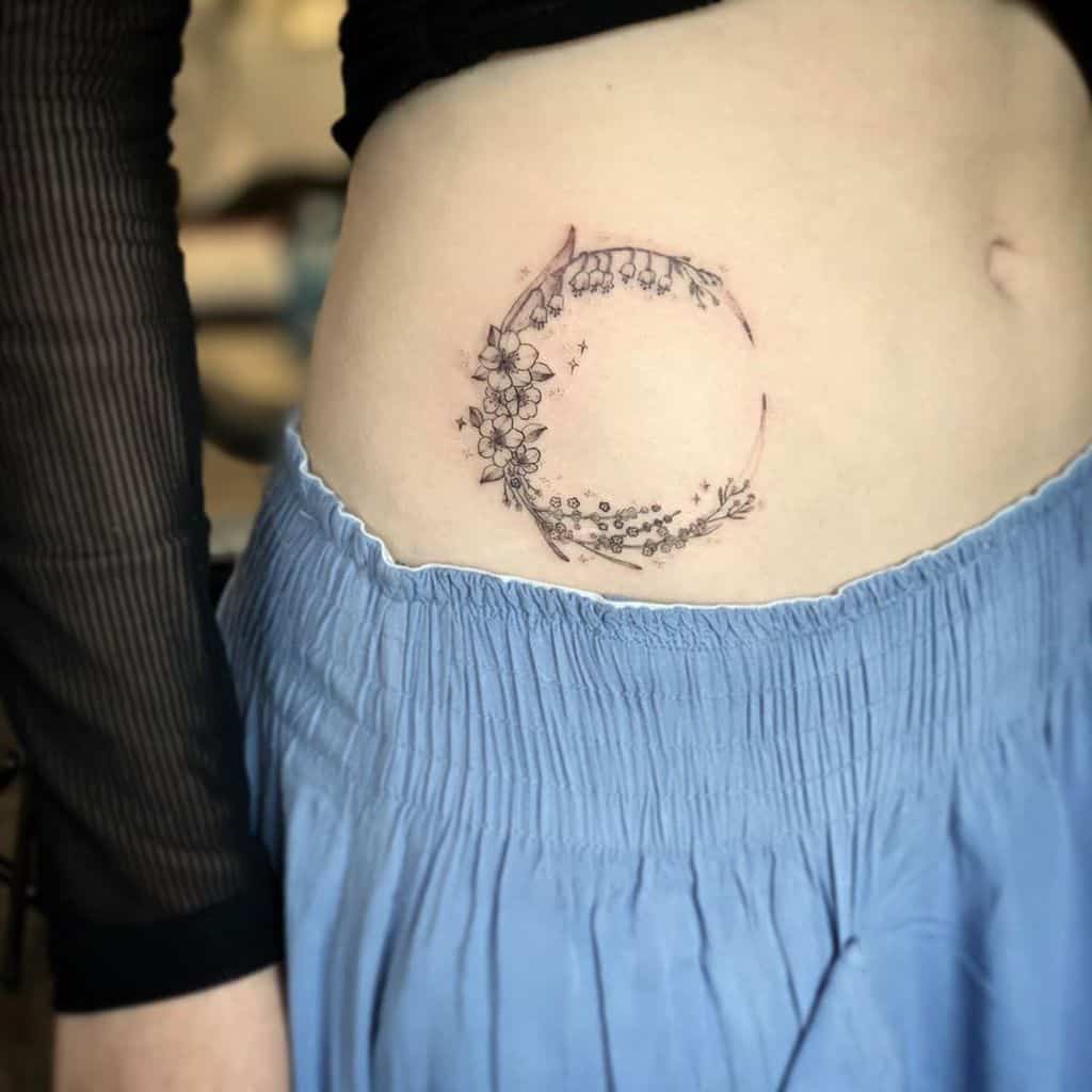 A tattoo of a crescent moon adorned with delicate flowers and stars, placed on the side of the abdomen.