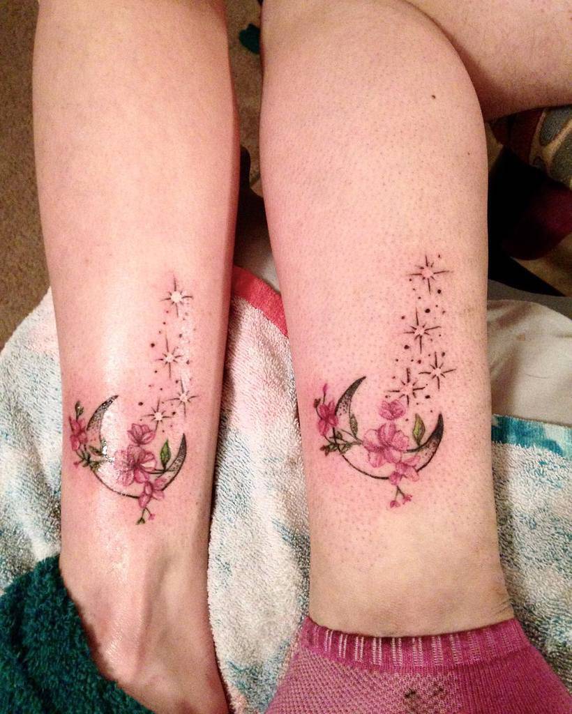 Matching mother-daughter tattoos of a crescent moon with pink flowers and stars