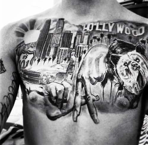 Chest tattoo featuring LA skyline, Hollywood sign, bear, lowrider car, and hands forming LA symbol in bold black and gray ink.