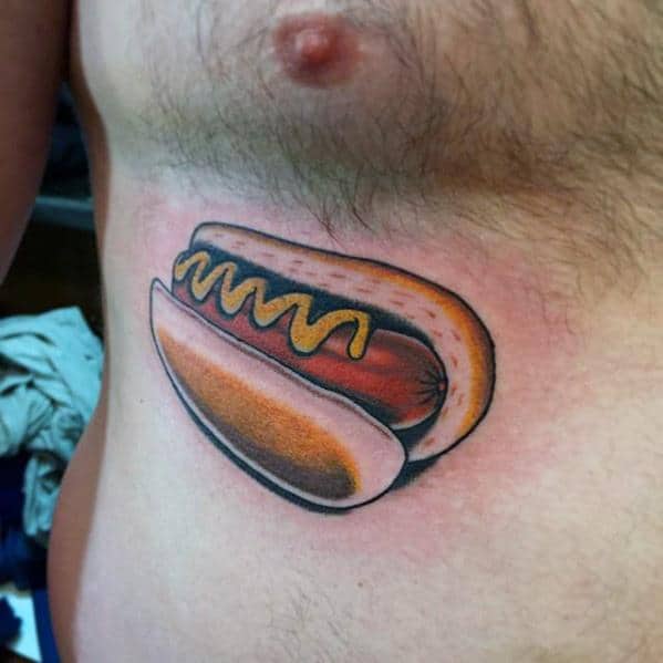 Hot dog tattoo featuring a sausage with mustard inside a split bun, located on the side of the torso.