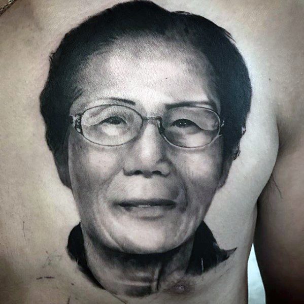 A realistic tattoo of an elderly woman wearing glasses, inked on a person's chest