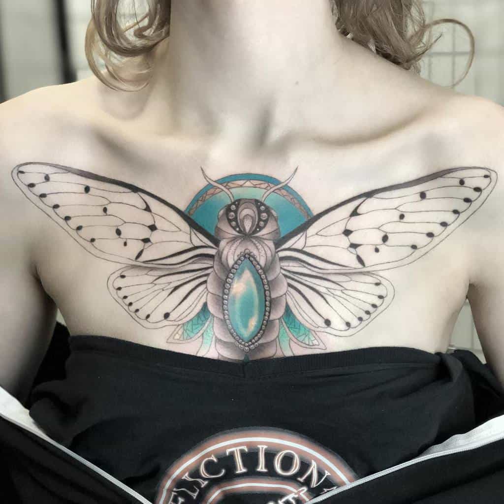 Intricate chest tattoo of a cicada with detailed wings and a vibrant teal gem-like body, accented by geometric patterns
