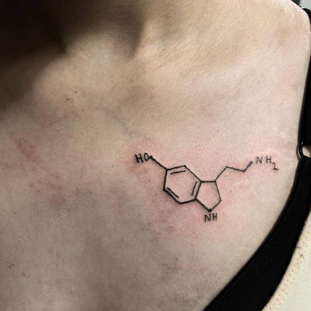 A chemical structure tattoo elegantly adorns the shoulder, depicting the serotonin molecule in minimalist black lines