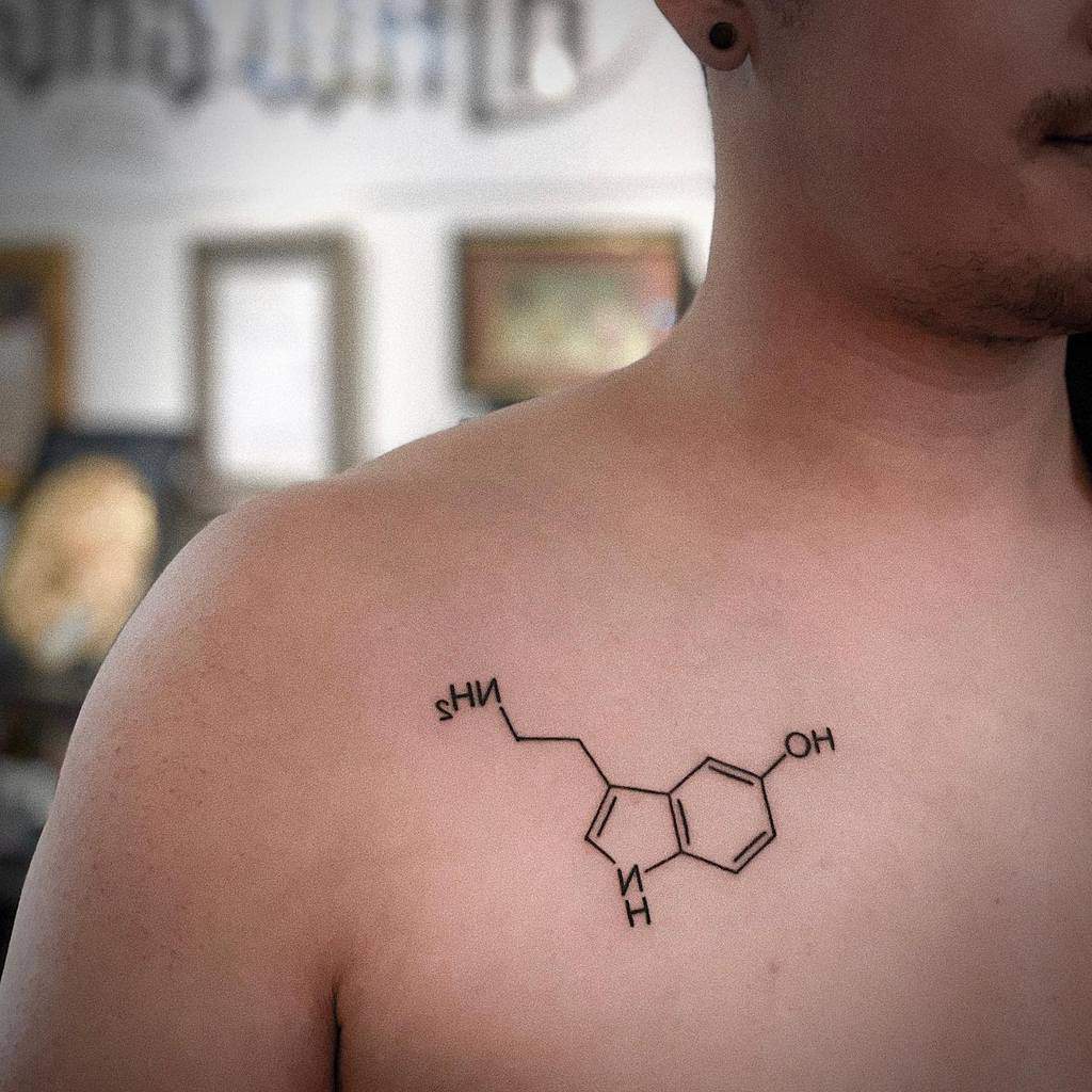 A beautifully intricate tattoo depicting the serotonin molecule graces the person's chest, symbolizing happiness and balance