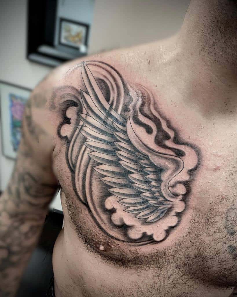 Close-up of a tattoo featuring a detailed wing design, surrounded by decorative shading and clouds