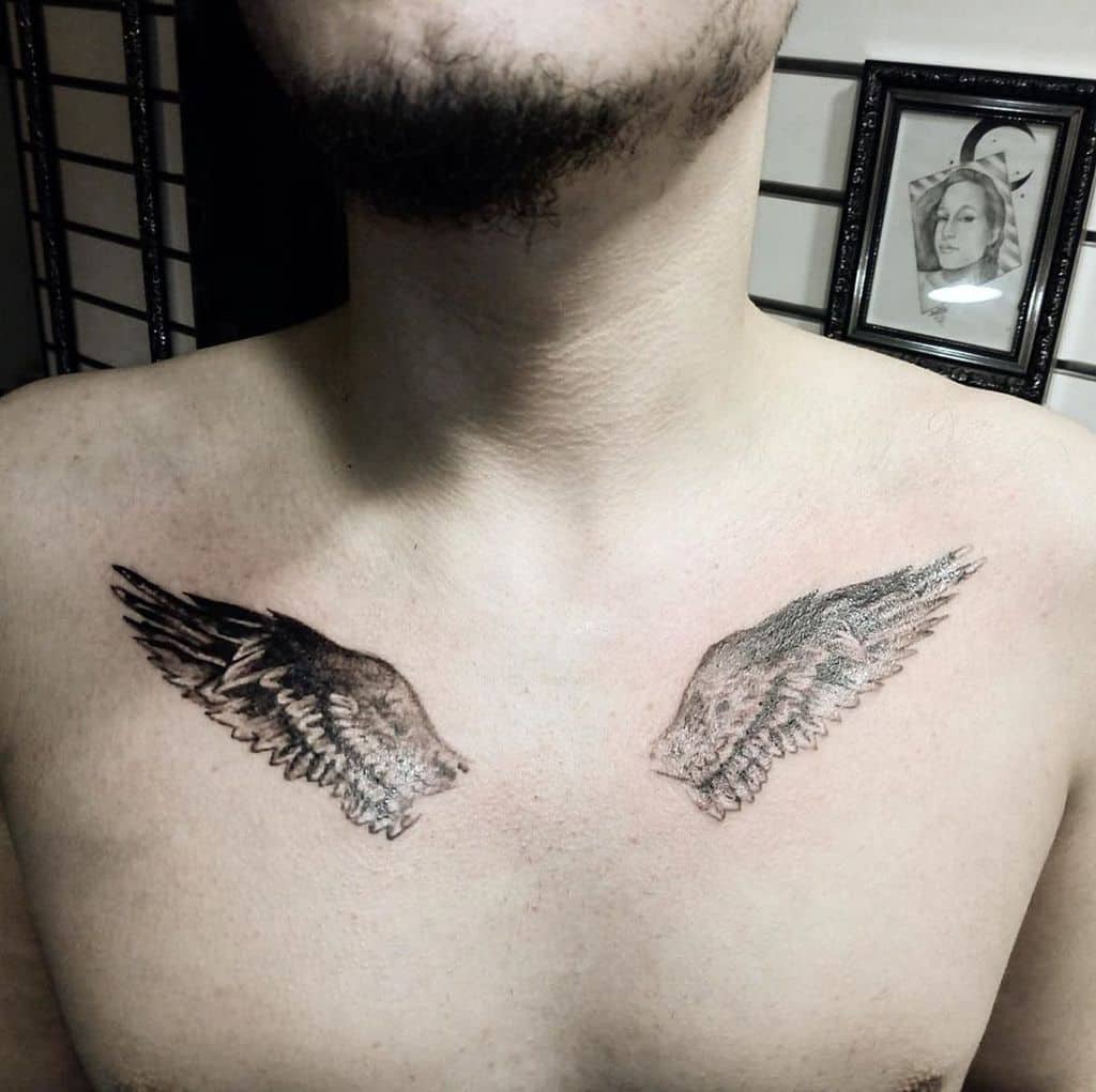 A tattoo of two realistic angel wings in black and grey ink with intricate shading