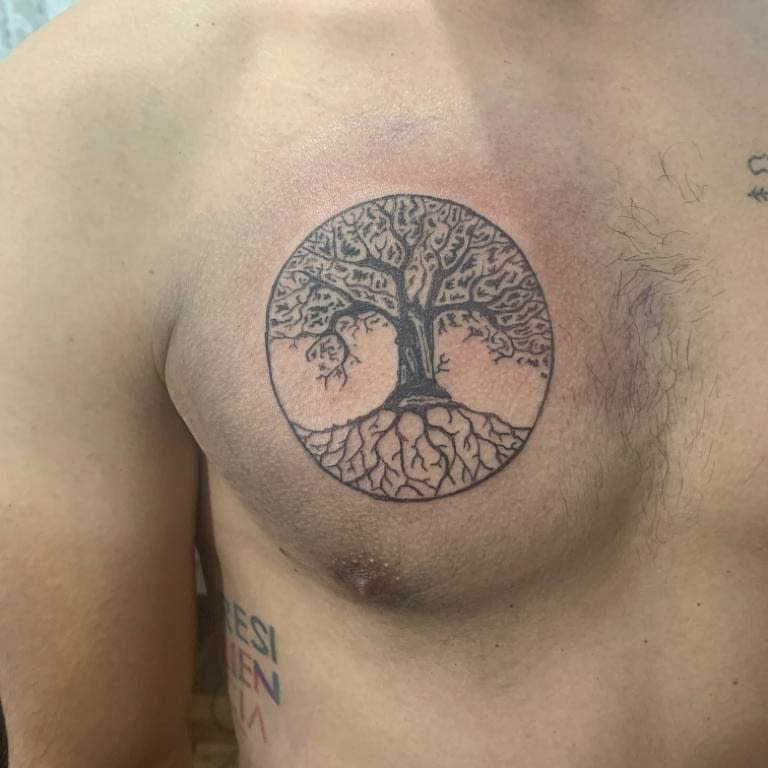 Chest tattoo featuring a circular tree of life design, showcasing intricate branches and roots to symbolize balance and connection
