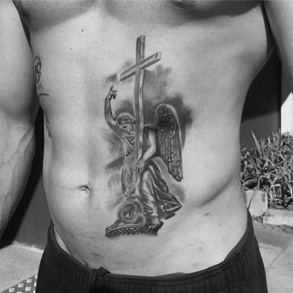 A detailed black and grey tattoo on the side of the torso, featuring an angel holding a cross and standing on a pedestal.