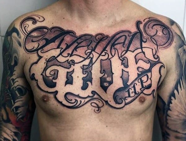 Chest tattoo for men featuring bold blackletter text and decorative script across the upper chest and shoulders.