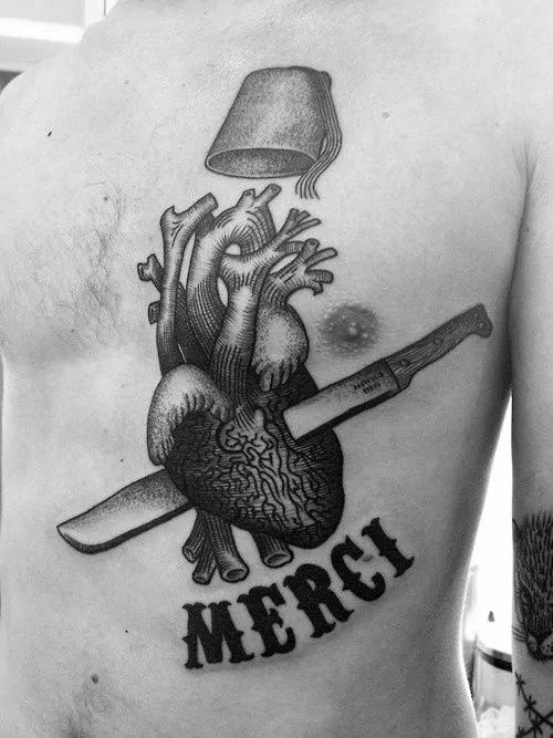 A black and gray tattoo of an anatomical heart pierced by a scalpel, with a bucket above and "MERCI" below