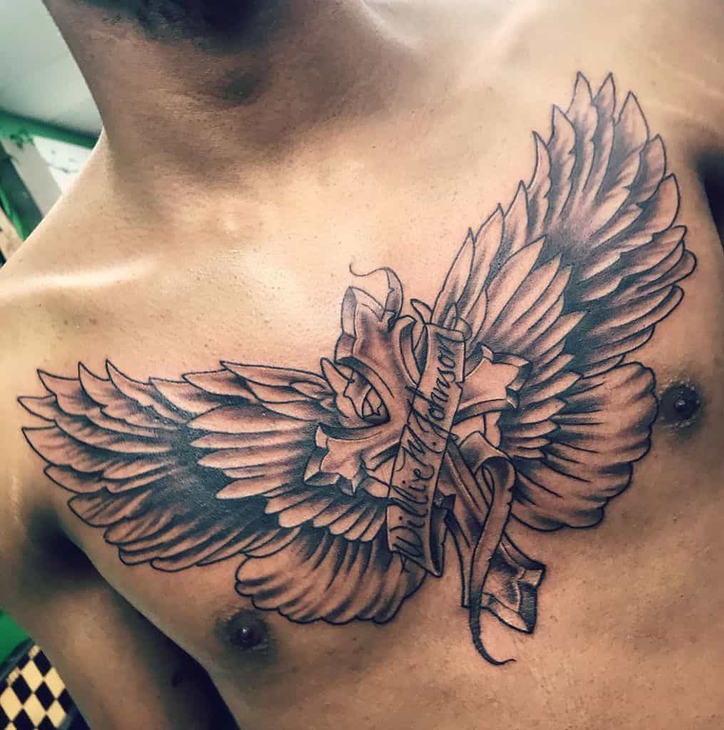 Bold tattoo featuring large angel wings wrapping around a cross with a banner displaying the name 'Willie M. Johnson'