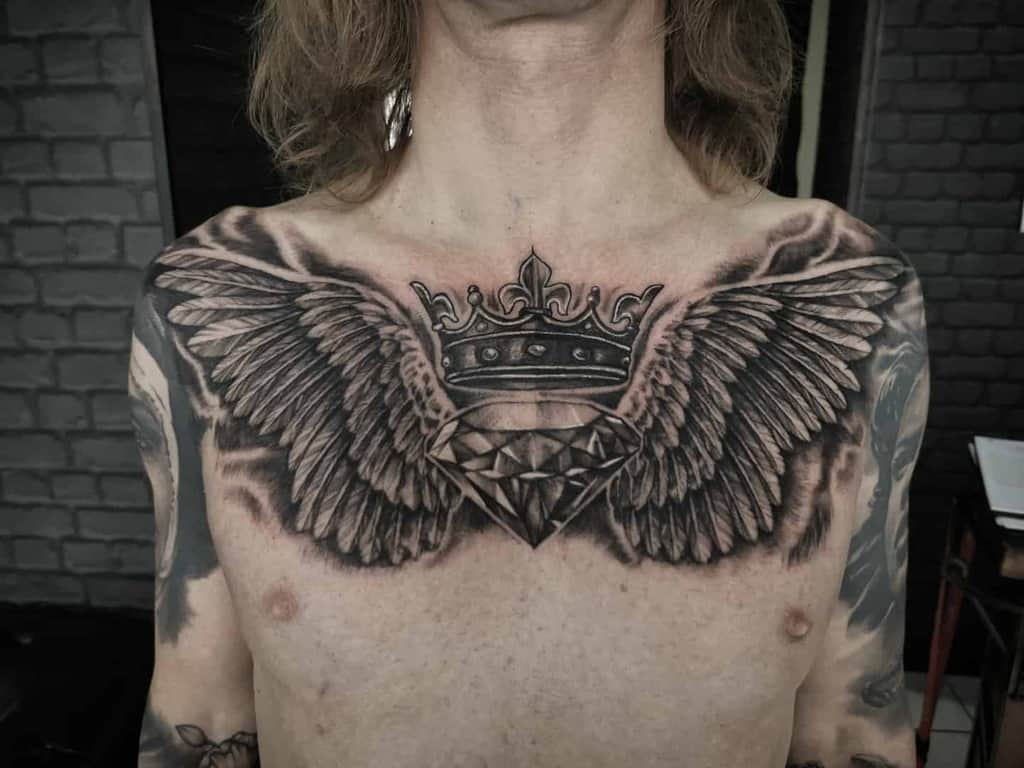 A black and grey tattoo of a crown, a spread angel wings, and a diamond