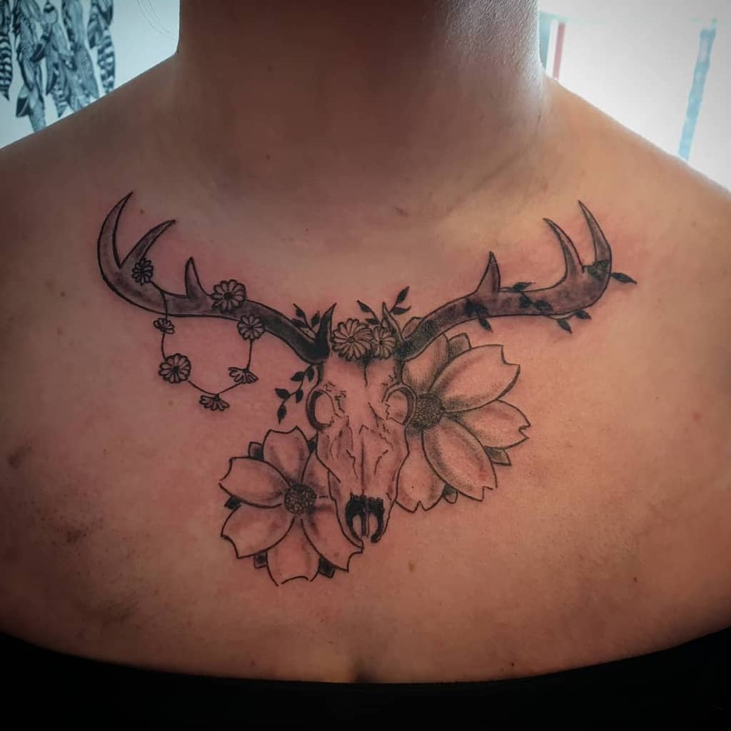 A chest tattoo featuring a striking deer skull adorned with floral antlers and two large flowers at its base