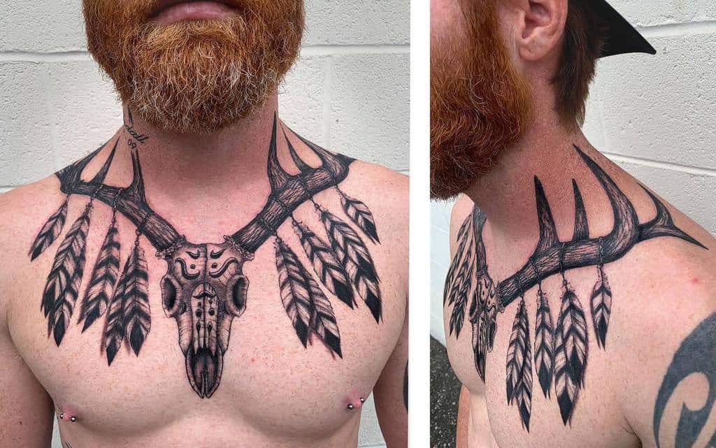 Large black upper chest tattoo featuring a deer skull adorned with feathers