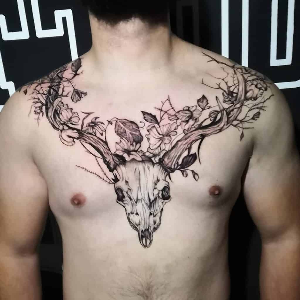 Chest tattoo showcasing a majestic deer skull with antlers adorned with delicate flowers, intertwining branches, and graceful birds