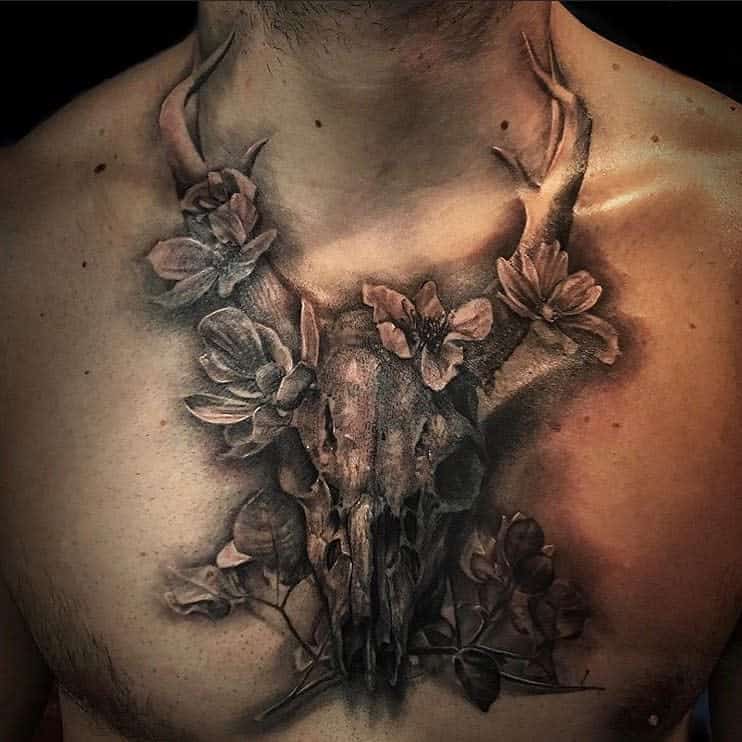 Chest tattoo of a deer skull with antlers, surrounded by intricate flowers and leaves
